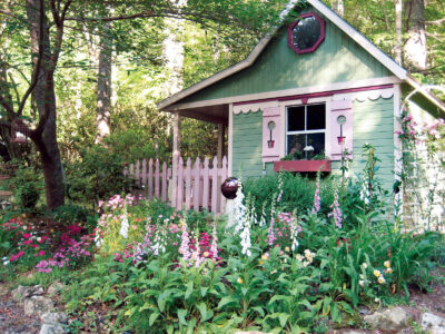 green shed with pink trim surrounded by trees and pink flowers